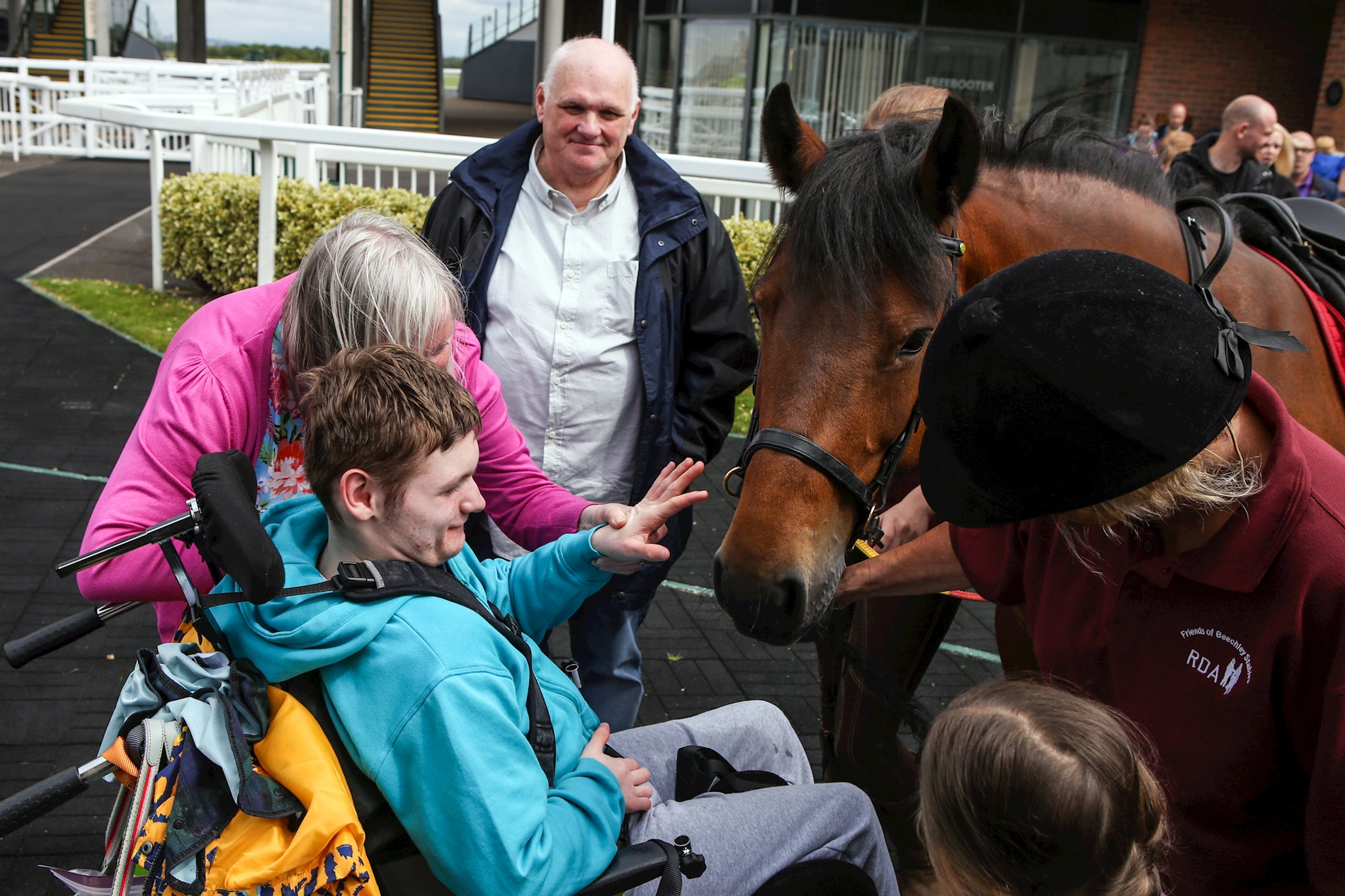 A young man in a wheelchair strokes a horse while attending a disabled riding lesson at Aintree Racecourse