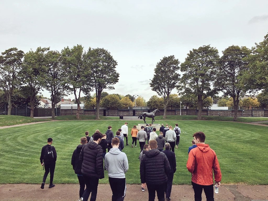 A group of school children walking towards the statue of Red Rum during a tour of Aintree Racecourse