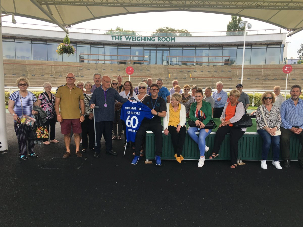 A group of people standing in the parade ring holding an Everton shirt up